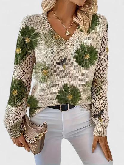 Damenpullover mit V-Ausschnitt, Blumenmuster und Strickdetails, kombiniert mit weißer Hose und beiger Handtasche. Modetrend Herbst 2023.