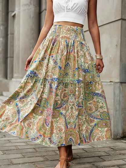 Frau in weißem Top und langem, buntem Boho-Rock mit Paisley-Muster, steht auf gepflastertem Weg vor steinernen Säulen.