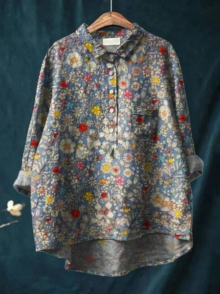Bluse mit Blumenmuster, langärmlig, aus Baumwolle, auf einem Kleiderbügel vor dunkelblauem Hintergrund. Ideal für Frühling und Sommermode.