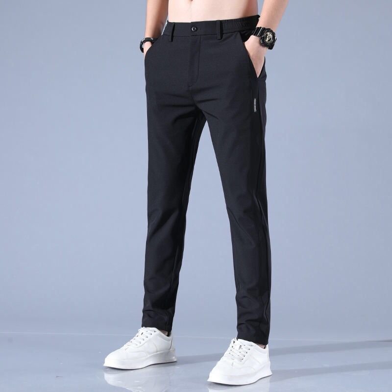 Mann trägt schwarze Slim-Fit-Hose und weiße Sneaker vor grauem Hintergrund. Modische Herrenbekleidung, elegante Hose, Freizeitlook.