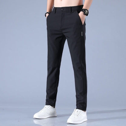 Mann trägt schwarze Slim-Fit-Hose und weiße Sneaker vor grauem Hintergrund. Modische Herrenbekleidung, elegante Hose, Freizeitlook.