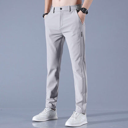 Graue Herren-Chinohose, modern geschnitten, mit elastischem Bund und Taschen, kombiniert mit weißen Sneakers. Ideal für Freizeitmode.