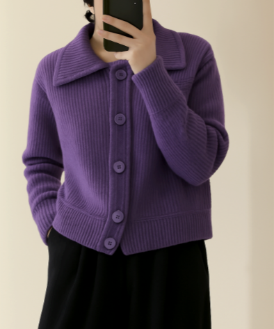 Frau in lila Strickjacke mit großen Knöpfen, hält Smartphone, trägt schwarze Hose. Modetrend, Herbstmode, Damenbekleidung, stilvoller Look.