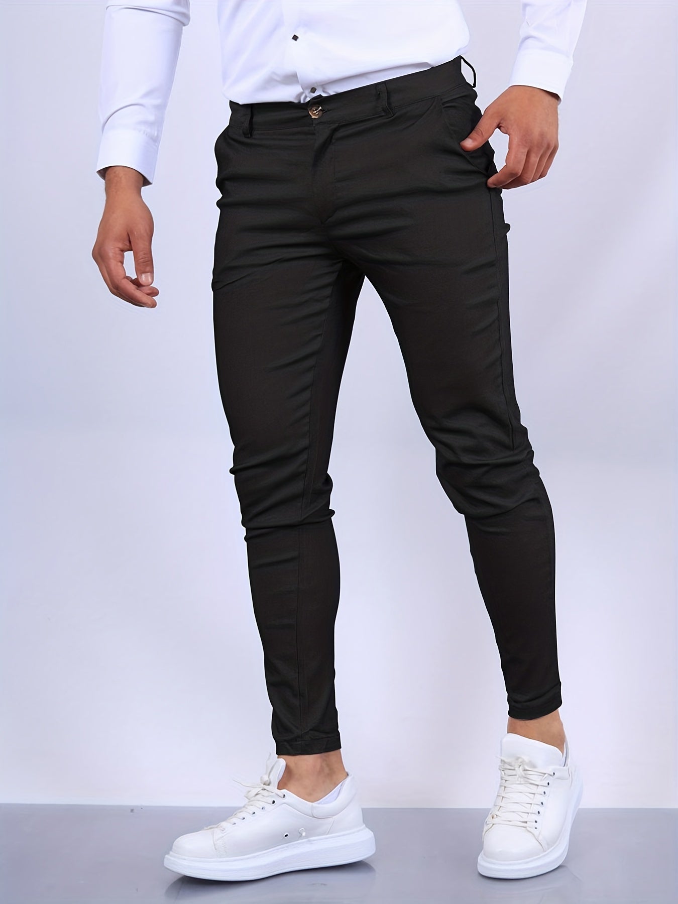 Mann in schwarzer Slim-Fit-Hose und weißen Sneakers, weißes Hemd. Mode für Herren, eleganter Look, moderne Kleidung, stilvolle Herrenmode.