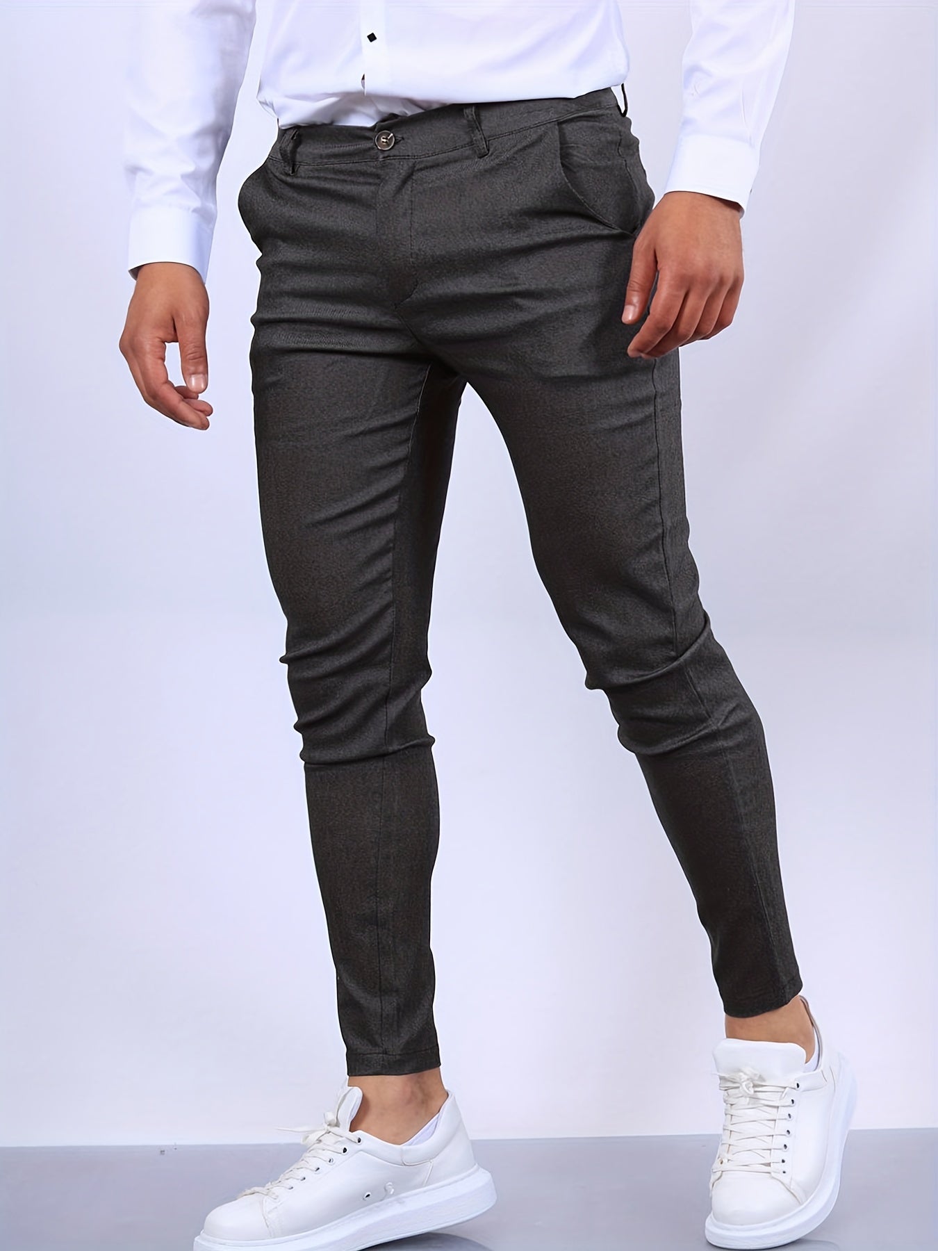 Mann in eleganter, grauer Anzughose und weißen Sneakers, trägt ein weißes Hemd. Mode für Herren, stilvolle Business- und Freizeitkleidung.