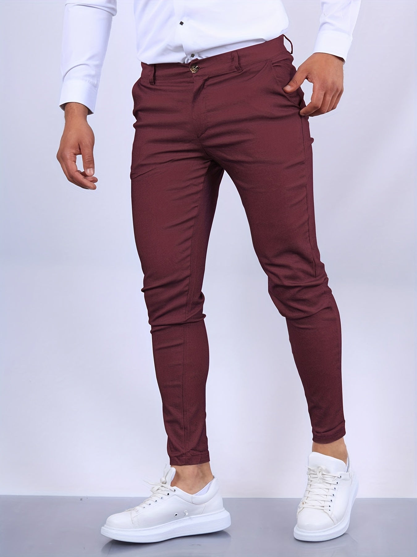 Mann in bordeauxroter Slim-Fit-Hose und weißem Hemd, kombiniert mit weißen Sneakern. Elegante Herrenmode, moderne Freizeitkleidung.