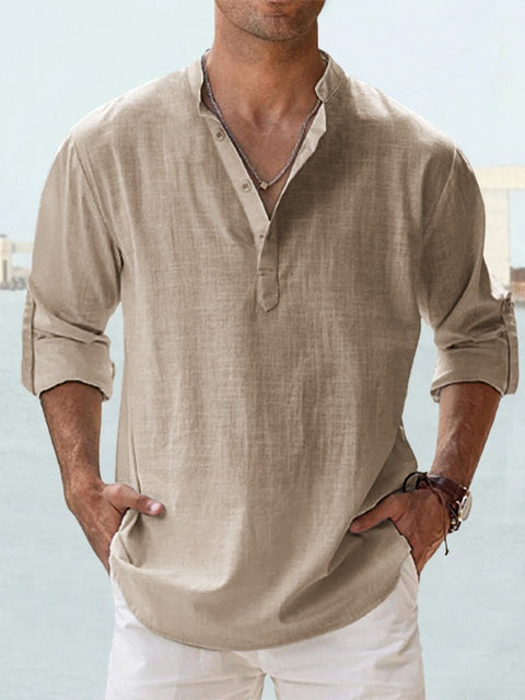 Mann trägt beiges Leinenhemd mit Stehkragen und Knopfleiste, kombiniert mit weißen Hosen. Lässige Sommermode, ideal für Strand oder Freizeit.