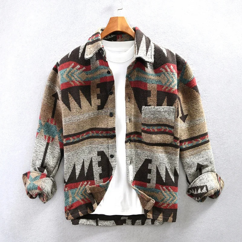 Bunte Azteken-Jacke mit geometrischem Muster, hängend an einem Holzkleiderbügel, über einem weißen T-Shirt. Modetrend, Herrenbekleidung, Herbststil.