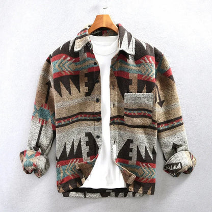 Bunte Azteken-Jacke mit geometrischem Muster, hängend an einem Holzkleiderbügel, über einem weißen T-Shirt. Modetrend, Herrenbekleidung, Herbststil.
