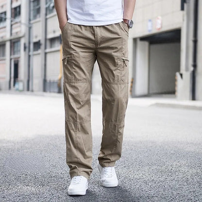 Mann in beigen Cargohosen und weißen Sneakers steht auf städtischer Straße. Moderne Herrenmode, lässiger Stil, urbane Umgebung.