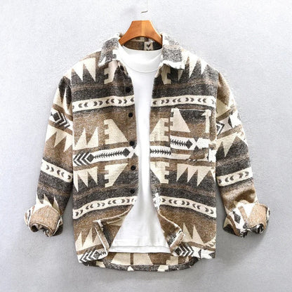 Braune Azteken-Jacke mit geometrischem Muster, hängend auf Holzkleiderbügel, über weißem T-Shirt. Modetrend, Herrenbekleidung, Herbstmode.