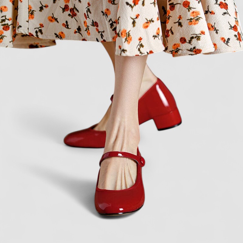 Rote Lackleder-Mary-Jane-Schuhe mit Blockabsatz, getragen von einer Person in einem geblümten Rock. Elegante Damenschuhe, modisch und klassisch.