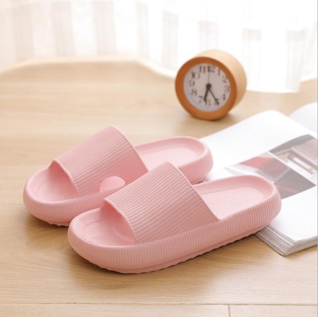 Rosa Badeschlappen auf Holzboden neben Wecker und Magazin. Bequeme, rutschfeste Hausschuhe für Damen. Ideal für Badezimmer oder Strand.