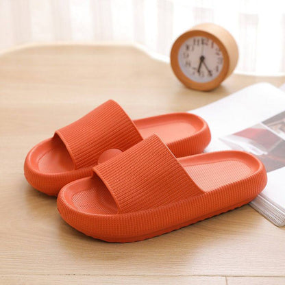 Orange Badeschlappen auf Holztisch, neben Wecker und Buch. Bequeme, rutschfeste Hausschuhe, ideal für Badezimmer oder Strand.