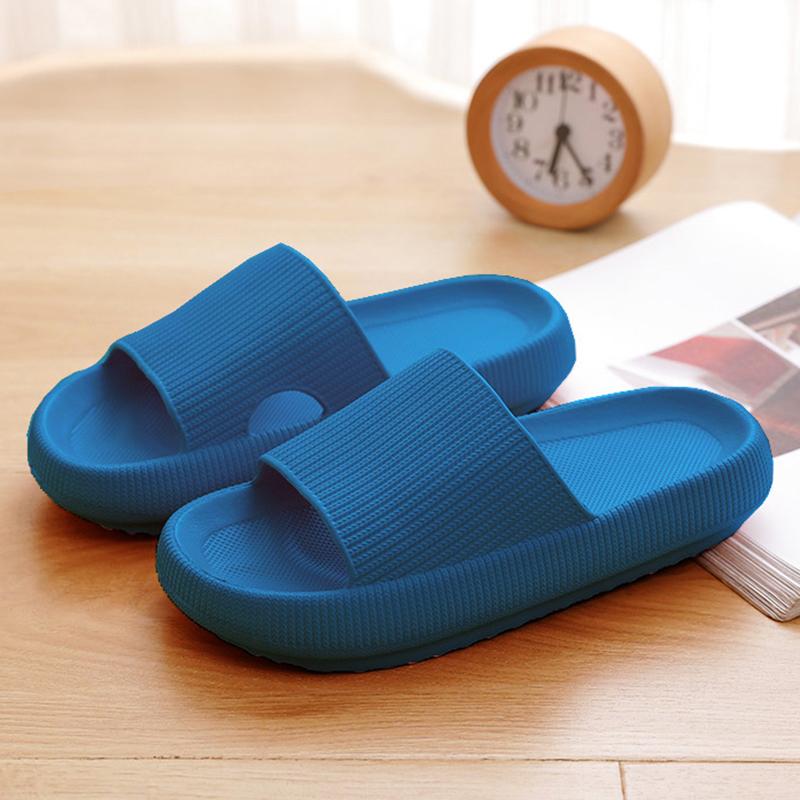Blaue Badeschlappen auf Holzboden, neben einer Uhr und Zeitschrift. Bequeme, rutschfeste Hausschuhe für Damen und Herren. Ideal für Zuhause.