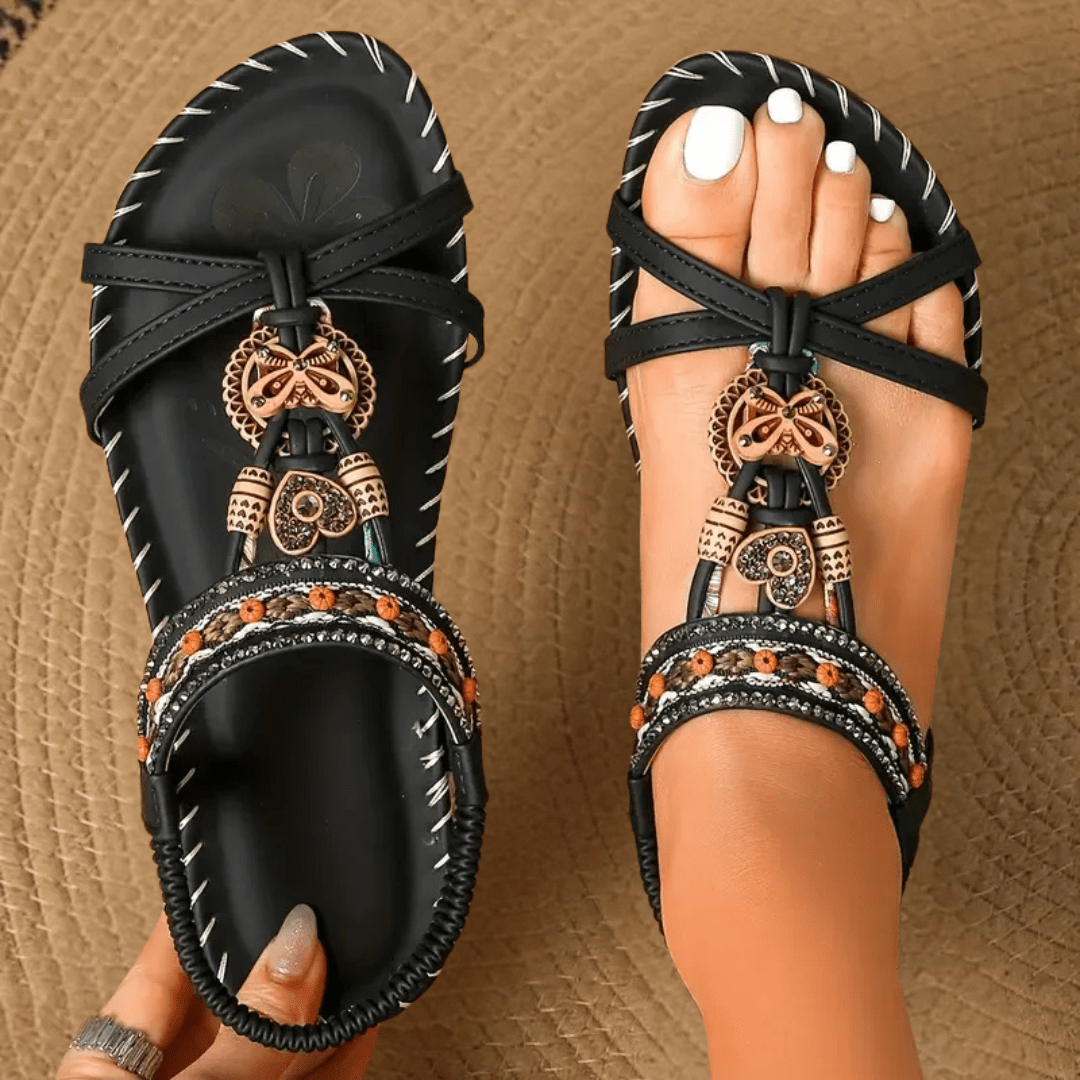 Schwarze Sandalen mit ethnischen Verzierungen und Perlen, getragen auf einem geflochtenen Teppich. Modische Sommerschuhe für Damen.