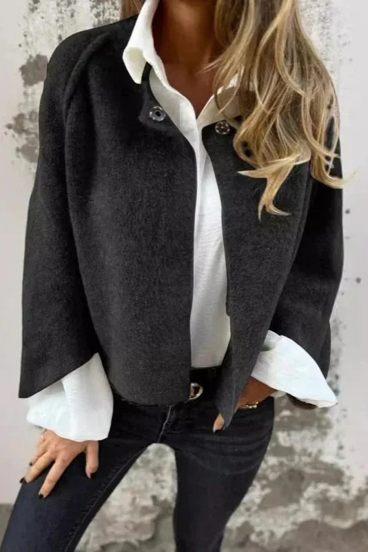 Frau in schwarzer Jacke und weißer Bluse vor grauer Wand. Modetrend, elegante Damenbekleidung, lässiger Stil, Herbstmode.
