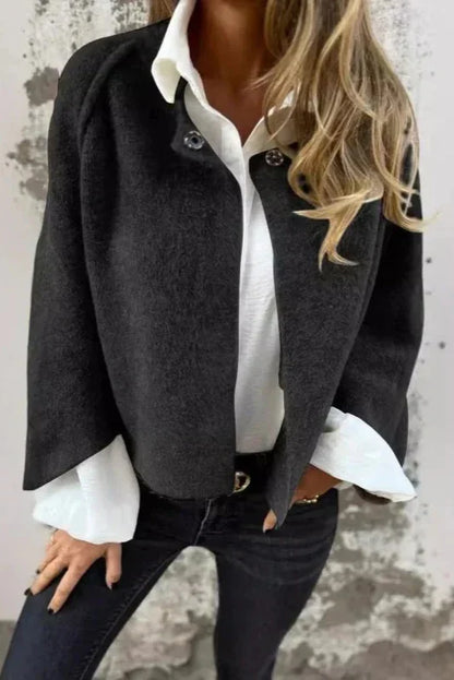 Frau in schwarzer Jacke und weißer Bluse vor grauer Wand. Modetrend, elegante Damenbekleidung, lässiger Stil, Herbstmode.