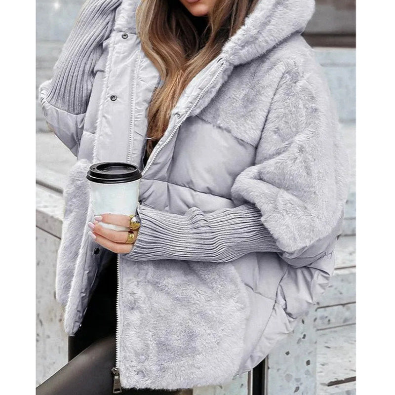 Frau in grauem, flauschigem Wintermantel mit Kapuze hält einen Kaffeebecher. Modetrend, Wintermode, Damenbekleidung, gemütlicher Look.