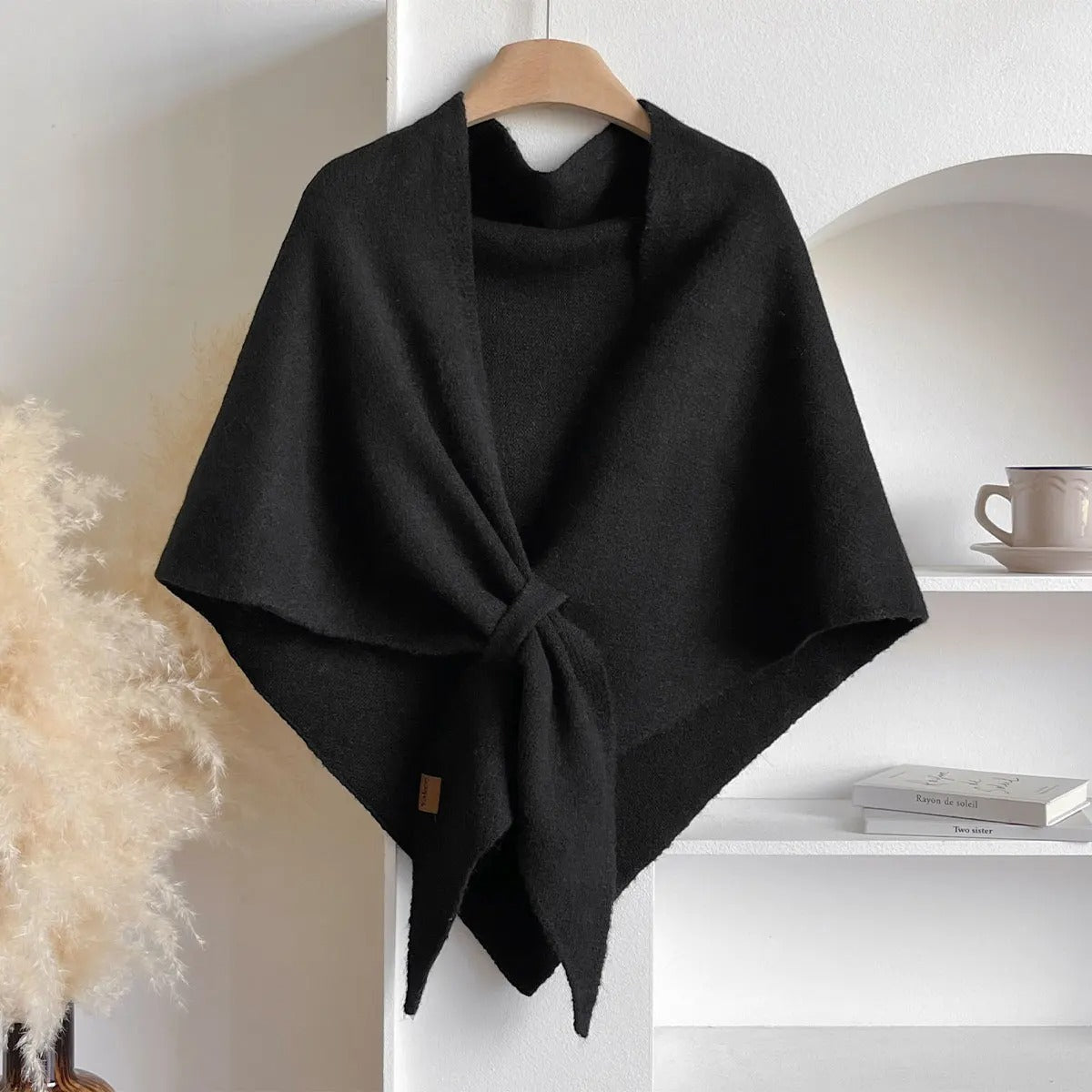Schwarzer Wollponcho auf Kleiderbügel, minimalistisch, elegant, Herbstmode, Damenbekleidung, gemütlich, stilvoll, modernes Design, Wohnzimmerdekor.