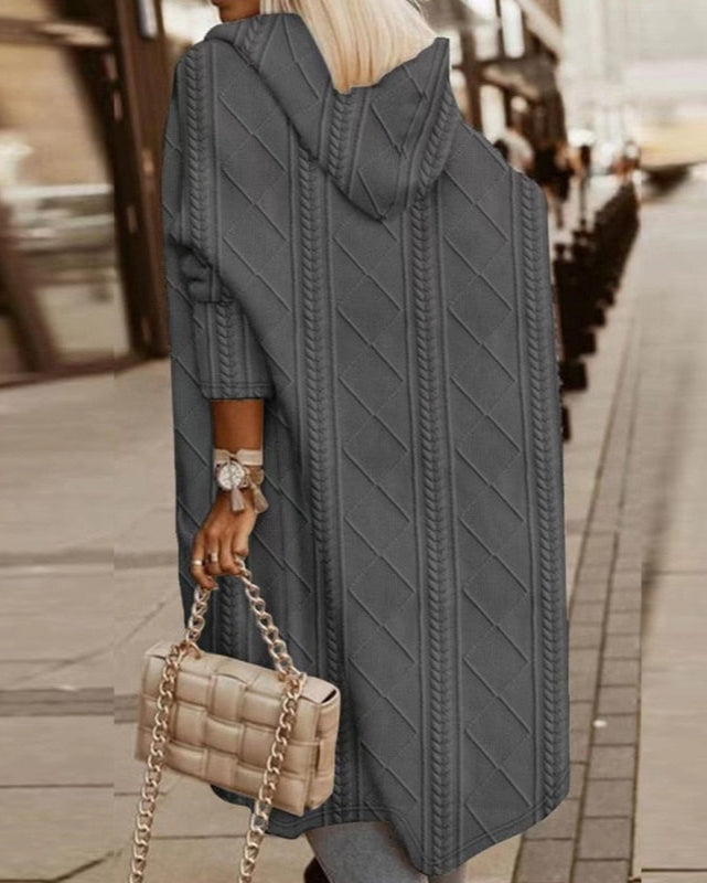 Frau in grauem Strickmantel mit Kapuze, hält beige gesteppte Handtasche mit Kettengriff. Modetrend Herbst, Straßenmode, stilvoller Look.