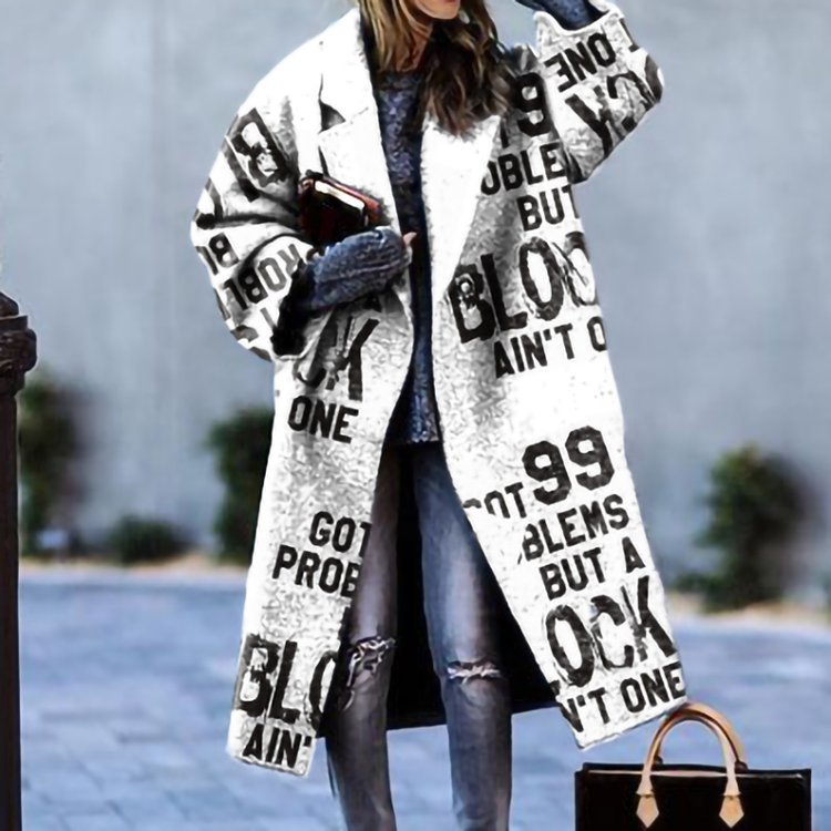 Frau trägt langen weißen Mantel mit schwarzem Textmuster, lässiger Streetstyle, modische Jeans, grauer Pullover, trendige Herbstmode.