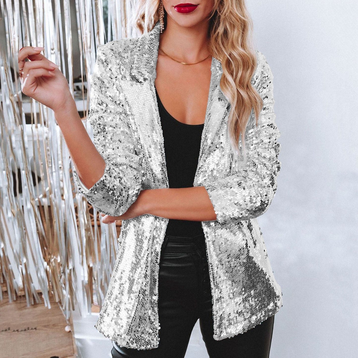Frau in silbernem Paillettenblazer, schwarzem Top und Lederhose vor glitzerndem Hintergrund. Elegante Mode, glamouröser Look, Party-Outfit.